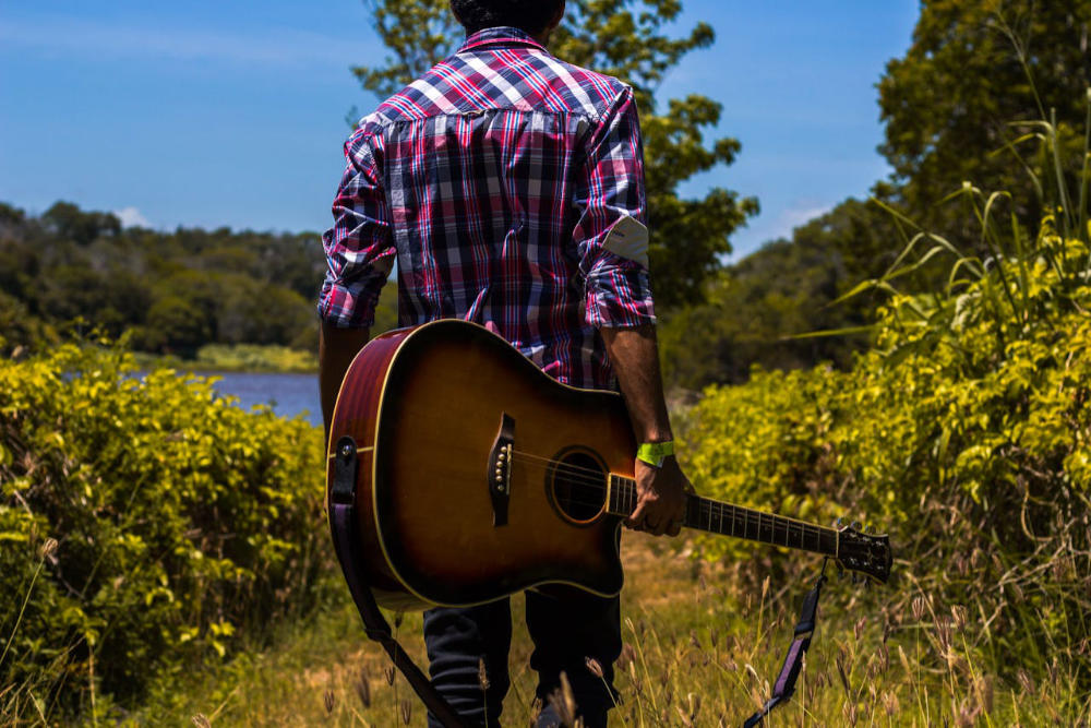 man standing in nature with a guitar